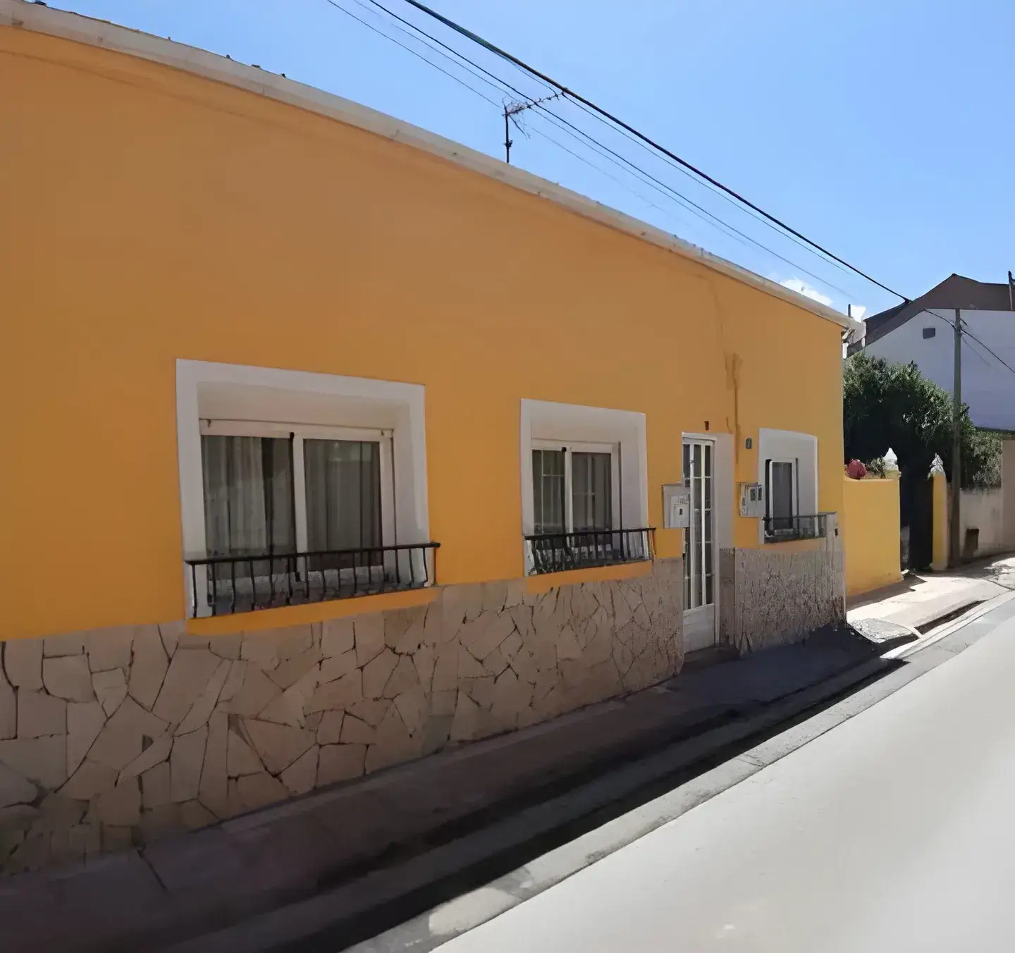 Los Pintores en Granada Fachada de casa tradicional pintada en color amarillo con zócalo de piedra